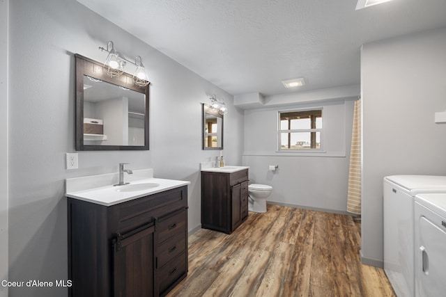 full bathroom with washer and clothes dryer, toilet, a sink, two vanities, and wood finished floors
