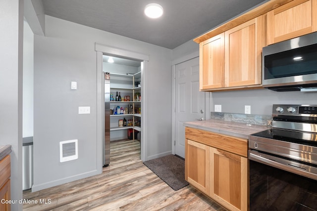 kitchen featuring light countertops, light wood-type flooring, stainless steel appliances, light brown cabinets, and visible vents