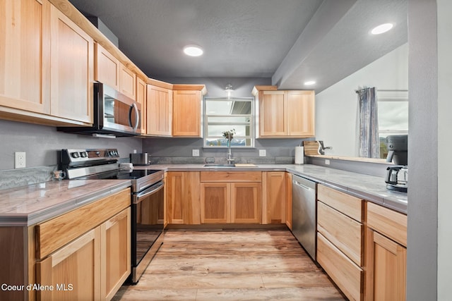 kitchen with a sink, stainless steel appliances, light brown cabinetry, and light wood-style floors