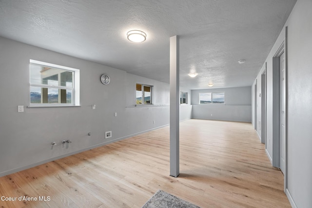 below grade area featuring plenty of natural light, baseboards, light wood-style floors, and a textured ceiling