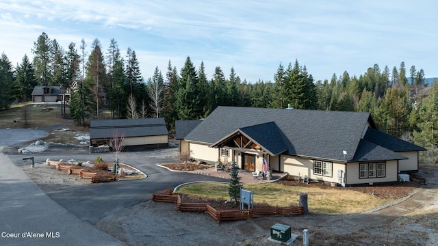 view of front of home featuring a wooded view and a shingled roof