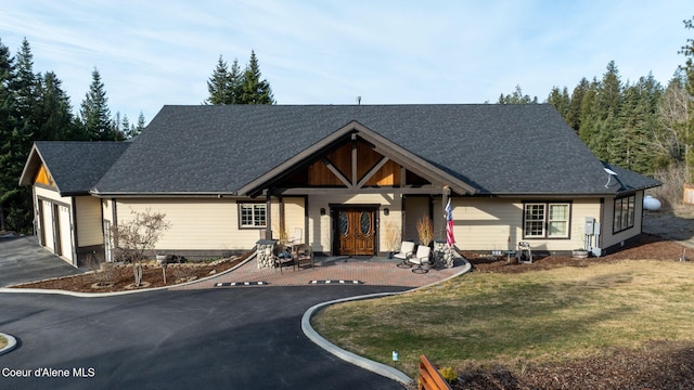 view of front of property featuring aphalt driveway, a garage, a front lawn, and a shingled roof