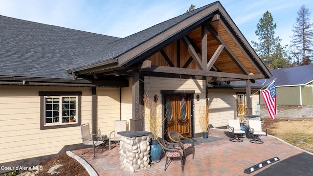 property entrance with a patio area and roof with shingles