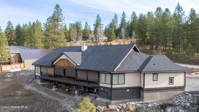 back of house featuring a deck, a chimney, and a shingled roof