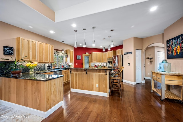 kitchen featuring arched walkways, dark wood-type flooring, a breakfast bar area, and light brown cabinetry