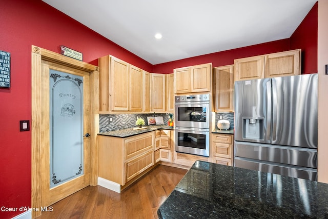 kitchen with light brown cabinetry, decorative backsplash, dark stone countertops, stainless steel appliances, and dark wood-style flooring