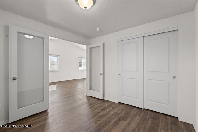 unfurnished bedroom featuring a closet, baseboards, a textured ceiling, and dark wood-style flooring