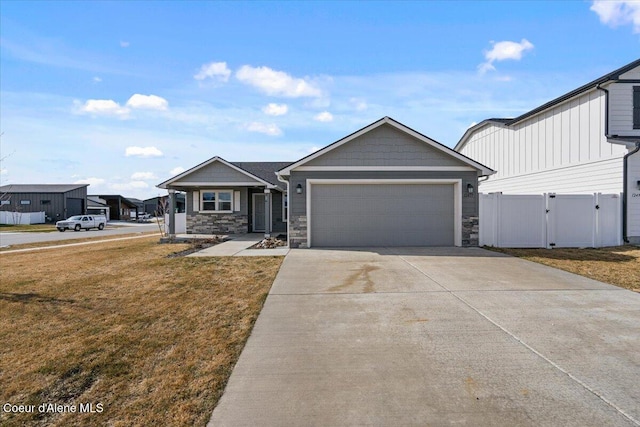 view of front of property featuring a front yard, fence, driveway, an attached garage, and stone siding