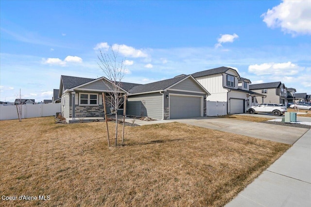 view of front of house with an attached garage, a front lawn, fence, stone siding, and driveway