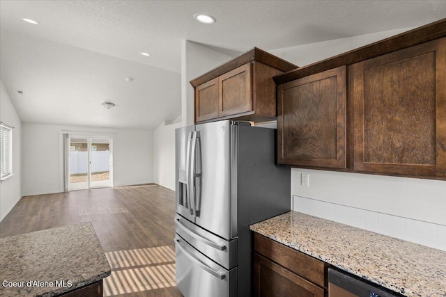 kitchen with dark brown cabinets, vaulted ceiling, light stone counters, wood finished floors, and stainless steel appliances