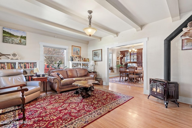 living area featuring an inviting chandelier, beamed ceiling, light wood-style flooring, and a wood stove