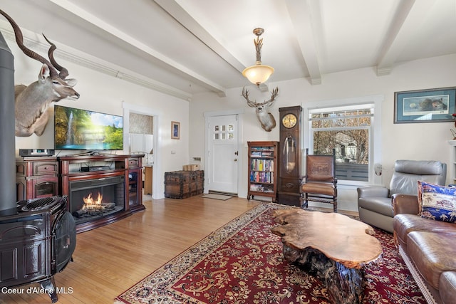 living area featuring beamed ceiling, light wood finished floors, and a warm lit fireplace