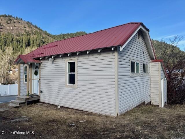 back of house featuring a mountain view, metal roof, an outdoor structure, and fence