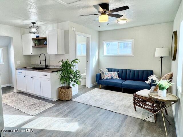 living area featuring ceiling fan, a textured ceiling, baseboards, and wood finished floors