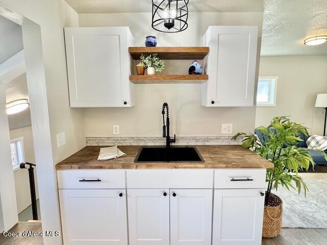 kitchen featuring open shelves, white cabinets, butcher block countertops, and a sink