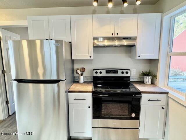 kitchen with under cabinet range hood, wood counters, wood finished floors, appliances with stainless steel finishes, and white cabinets