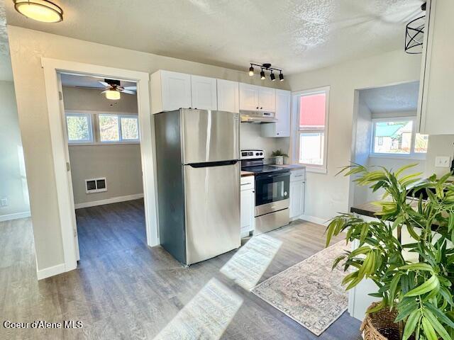 kitchen featuring baseboards, light wood-style flooring, stainless steel appliances, white cabinets, and under cabinet range hood