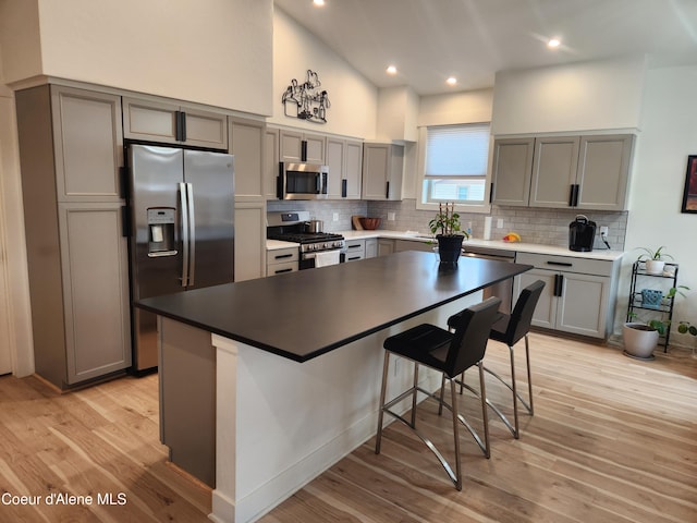 kitchen with gray cabinetry, light wood-style flooring, backsplash, stainless steel appliances, and a breakfast bar area