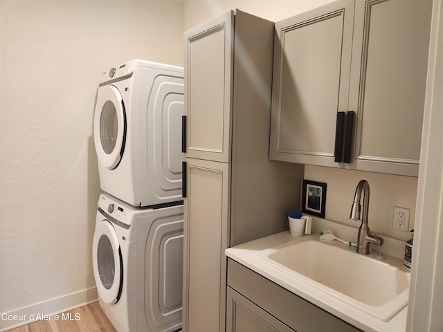 laundry room featuring a sink, wood finished floors, cabinet space, stacked washer / dryer, and baseboards