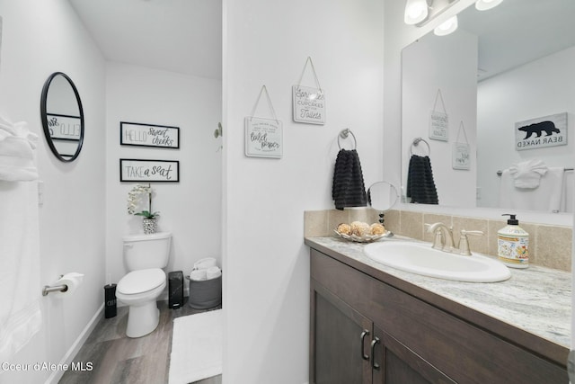 bathroom featuring baseboards, toilet, wood finished floors, and vanity