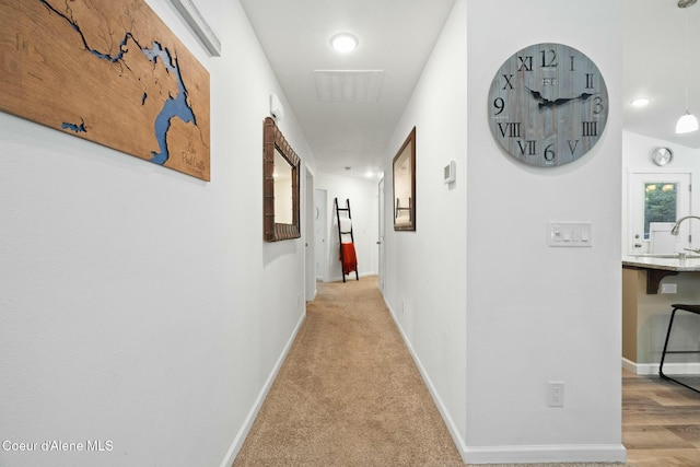 hall featuring baseboards, carpet floors, and a sink