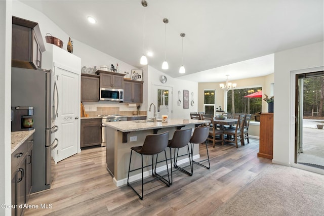 kitchen featuring light stone countertops, lofted ceiling, a sink, appliances with stainless steel finishes, and a kitchen bar