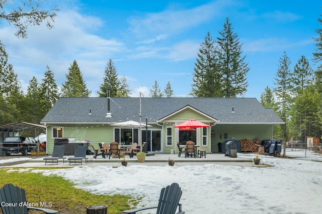 snow covered house featuring a carport and roof with shingles