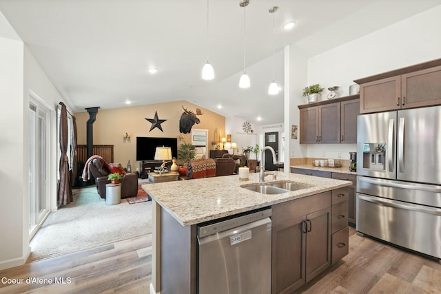 kitchen with light stone countertops, a sink, vaulted ceiling, light wood-style floors, and appliances with stainless steel finishes