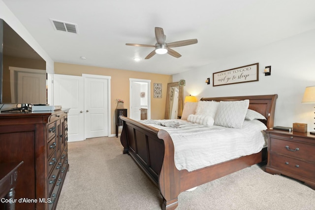 bedroom with a ceiling fan, light colored carpet, visible vents, and connected bathroom