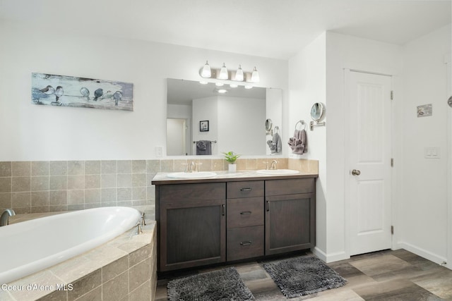 full bath featuring double vanity, wood finished floors, a garden tub, and a sink