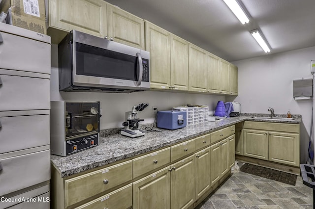 kitchen featuring stainless steel microwave, light stone countertops, stone finish flooring, and a sink