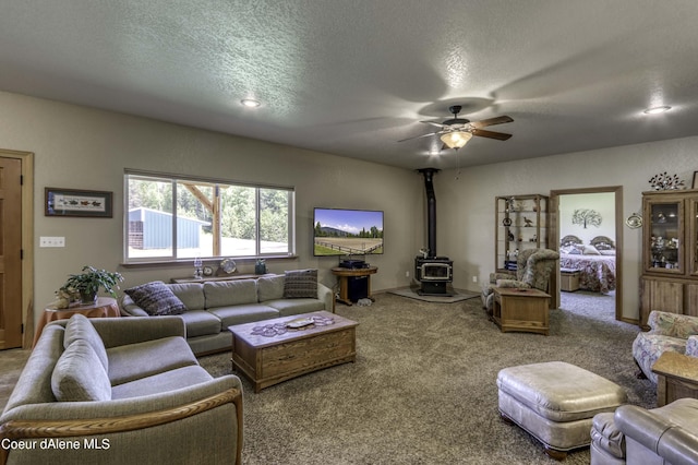 living room with carpet flooring, a textured ceiling, a wood stove, and a ceiling fan