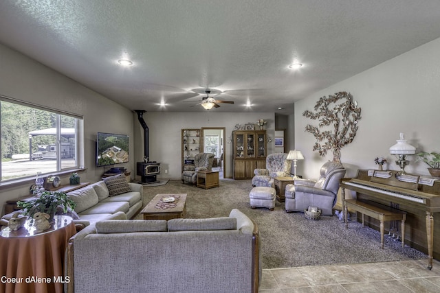 living room featuring carpet flooring, a textured ceiling, a wood stove, and ceiling fan