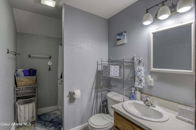 full bath featuring vanity, toilet, a textured wall, and baseboards