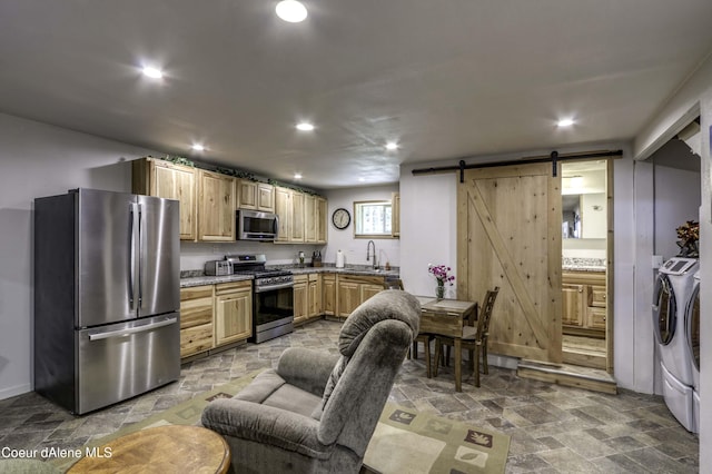 kitchen with stone finish flooring, washing machine and dryer, a barn door, stainless steel appliances, and a sink