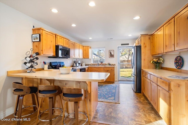 kitchen with a breakfast bar, a peninsula, recessed lighting, light countertops, and appliances with stainless steel finishes