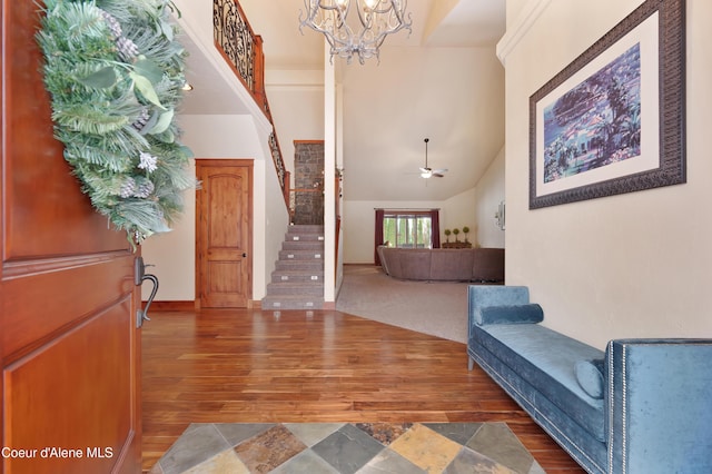 foyer featuring high vaulted ceiling, wood finished floors, stairs, and ceiling fan with notable chandelier