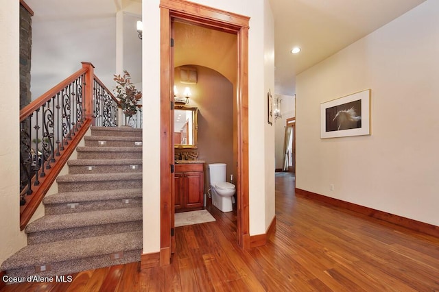 staircase with recessed lighting, wood finished floors, baseboards, and arched walkways