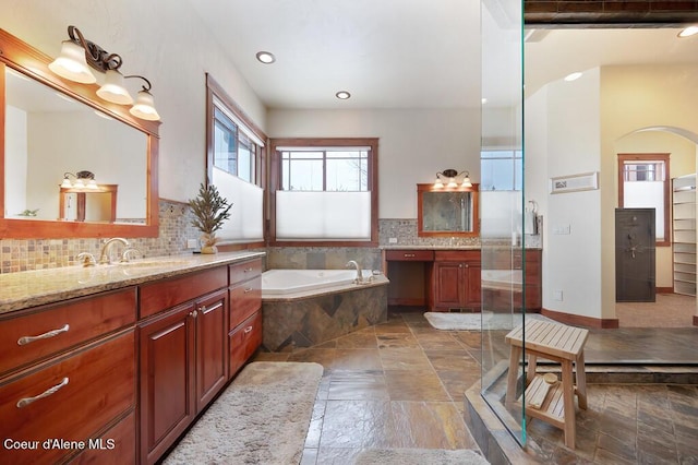 bathroom with vanity, stone tile flooring, a shower stall, a bath, and tasteful backsplash