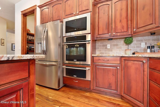 kitchen featuring tasteful backsplash, appliances with stainless steel finishes, light wood-type flooring, and light stone countertops