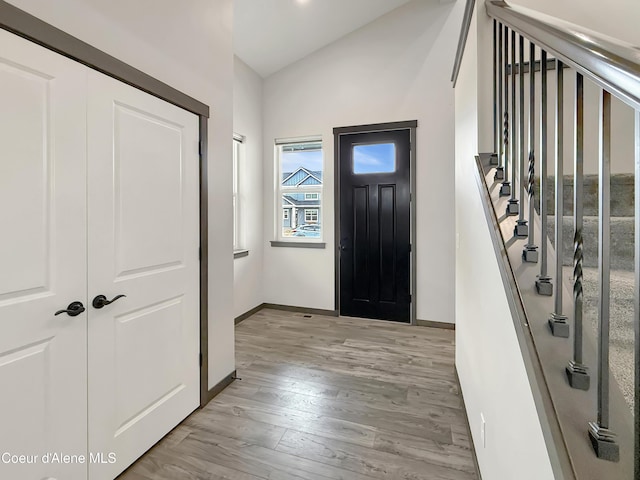 foyer entrance featuring stairway, baseboards, light wood-style floors, and vaulted ceiling