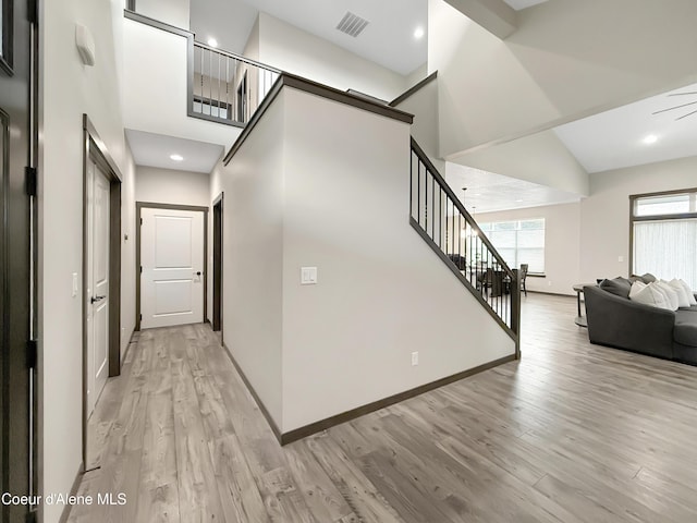 corridor featuring light wood finished floors, visible vents, stairway, and a towering ceiling