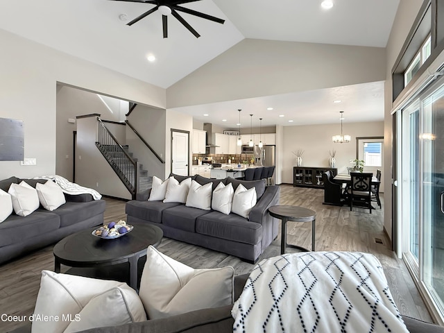 living area featuring stairway, recessed lighting, ceiling fan with notable chandelier, light wood-style floors, and high vaulted ceiling