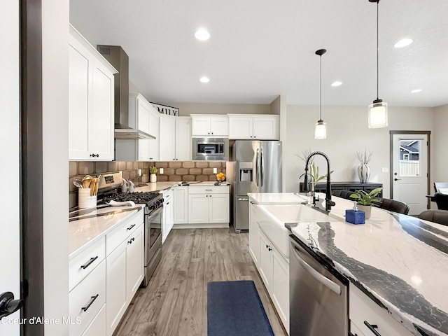 kitchen with tasteful backsplash, light stone counters, stainless steel appliances, wall chimney exhaust hood, and a sink