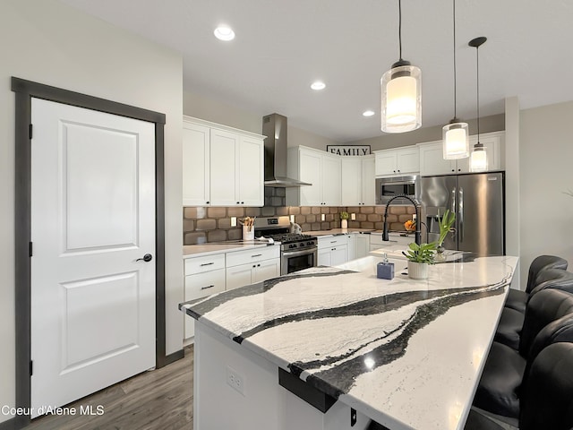 kitchen with wall chimney range hood, stainless steel appliances, white cabinets, pendant lighting, and a kitchen breakfast bar