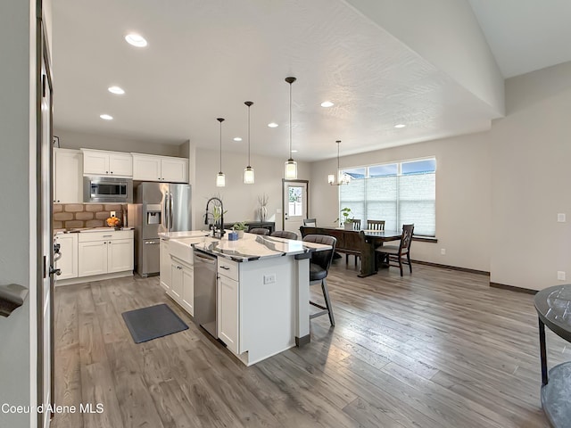 kitchen featuring a kitchen bar, decorative backsplash, appliances with stainless steel finishes, and light wood-type flooring