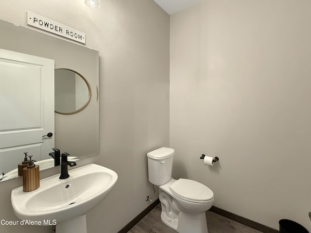 bathroom featuring toilet, wood finished floors, baseboards, and a sink