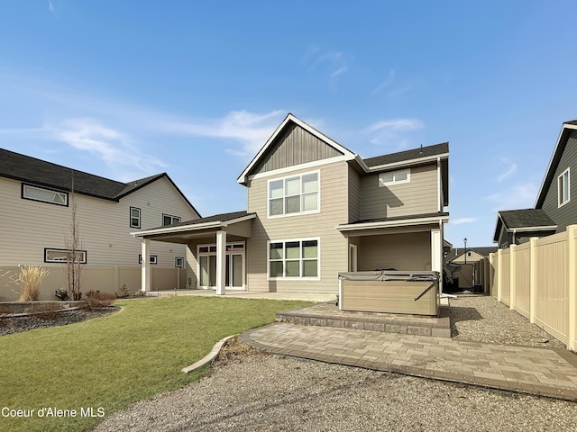 back of property with a hot tub, a fenced backyard, a yard, board and batten siding, and a patio area