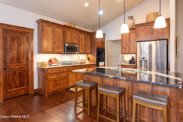 kitchen with brown cabinetry, appliances with stainless steel finishes, a kitchen breakfast bar, and dark wood-style flooring