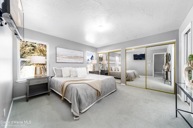 carpeted bedroom featuring baseboards, multiple closets, and a textured ceiling